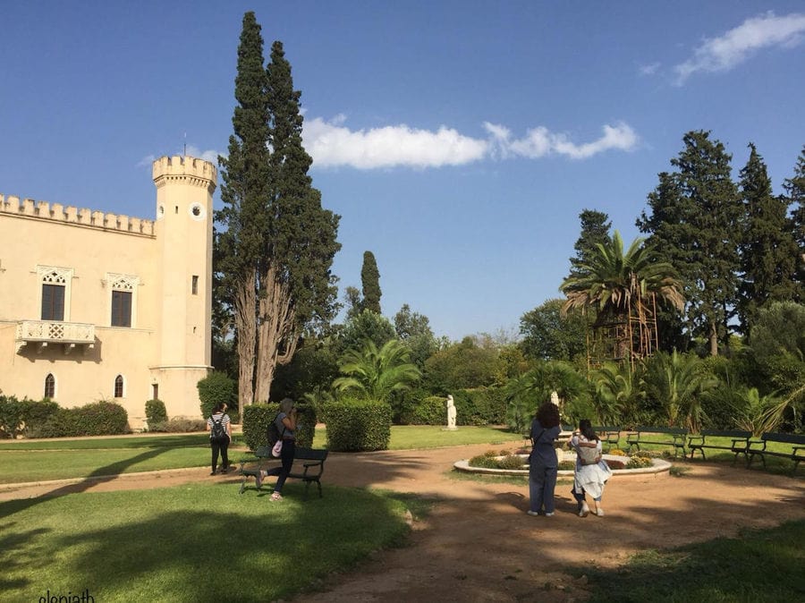 one side of the tall towers part of Pyrgos Vasilissis winery and tourists walking on the alleys' garden